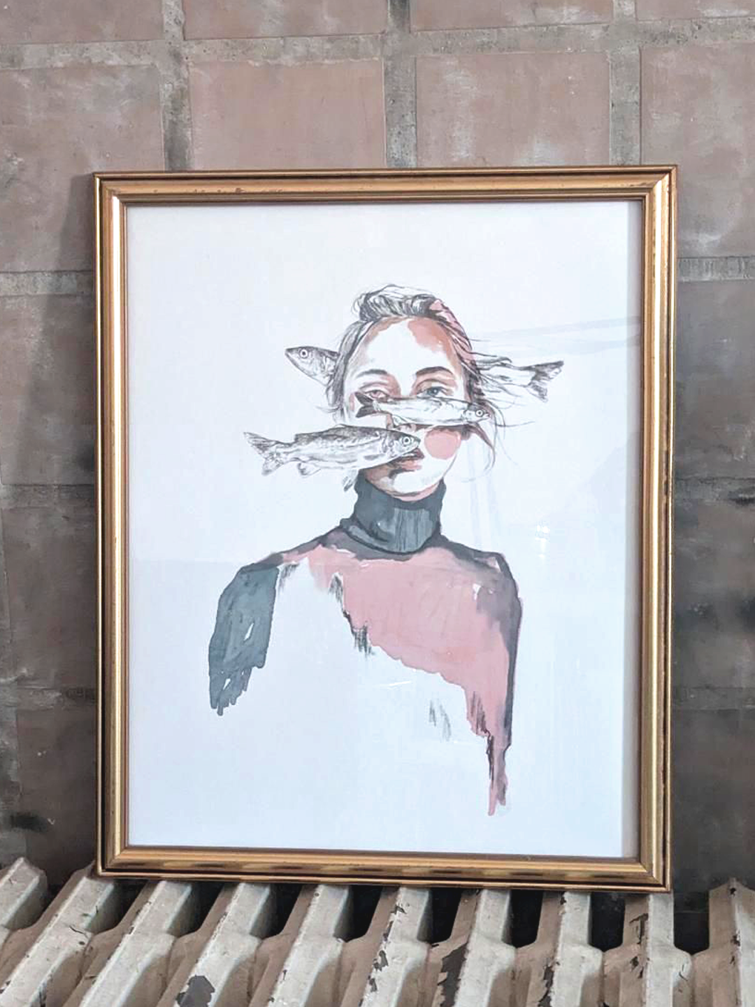 Framed artwork of a person with fish on their face against a brick wall. Artist: Joëlle Diane