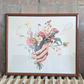 Framed artwork of a hand holding flowers on a radiator with a tiled wall background. Artist: Joëlle Diane
