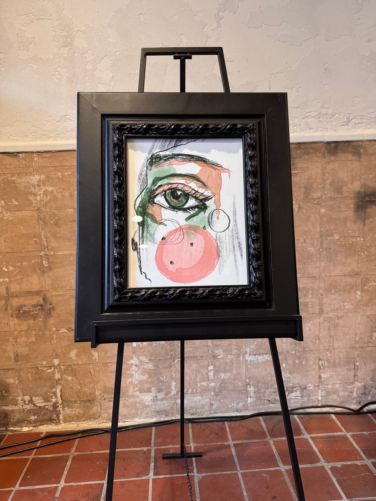 Artistic depiction of a face on a framed piece of art displayed on an easel against a textured wall. Focus on one eye. Artwork by Joëlle Diane of Monochrome Canvas.