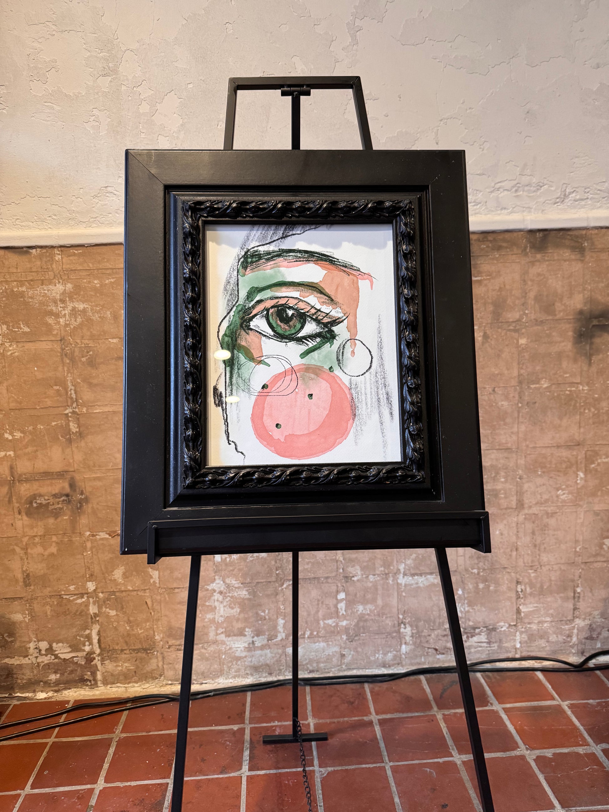 Artistic depiction of a face on a framed piece of art displayed on an easel against a textured wall. Focus on one eye. Artwork by Joëlle Diane of Monochrome Canvas.