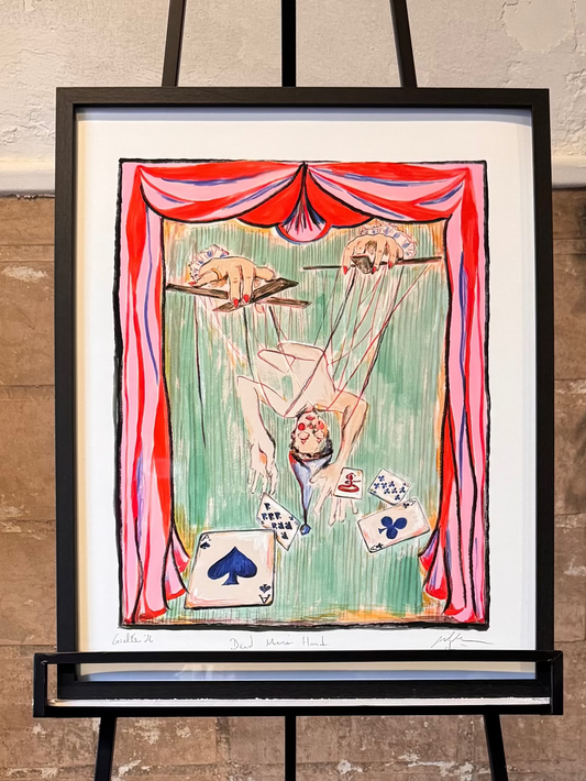 Artistic depiction of a circus performer tangled marionette with "Dead Man's Hand" poker cards, framed and displayed on an easel against a textured wall. Artwork by Joëlle Diane of Monochrome Canvas.
