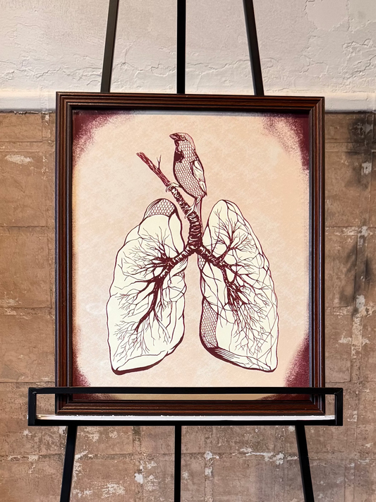 Anatomical lung with a song bird sitting atop it illustration on an easel against a textured wall.