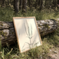Framed artwork of a black and white line drawing of culver's root leaning against a fallen log in a forest setting
